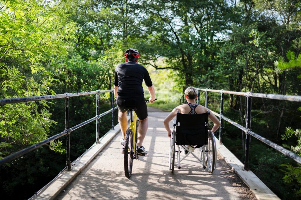 Man on a bike riding alongside a woman in a wheelchair